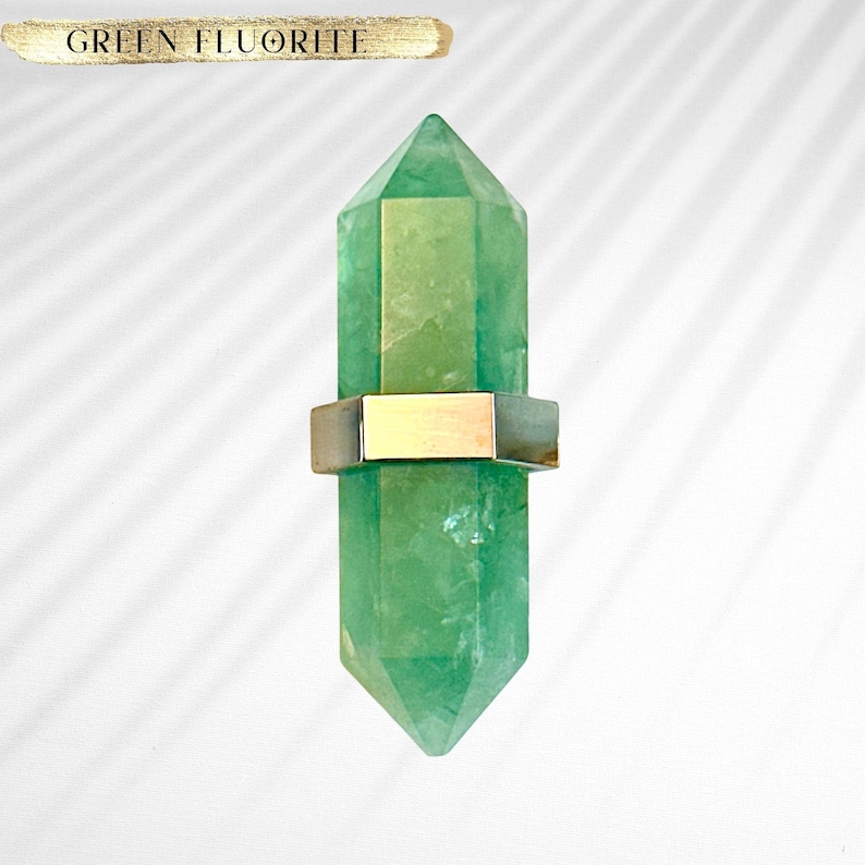 May include: A green fluorite crystal point with a gold metal band around the middle. The crystal is on a white background.