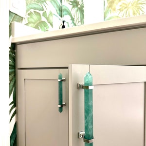 Green pulls on a bathroom vanity are made with green fluorite and solid brass hardware with a chrome finish. Tropical Versace wallpaper is on the bathroom wall of this designer Florida bathroom.