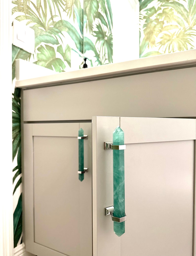 Green pulls on a bathroom vanity are made with green fluorite and solid brass hardware with a chrome finish. Tropical Versace wallpaper is on the bathroom wall of this designer Florida bathroom.