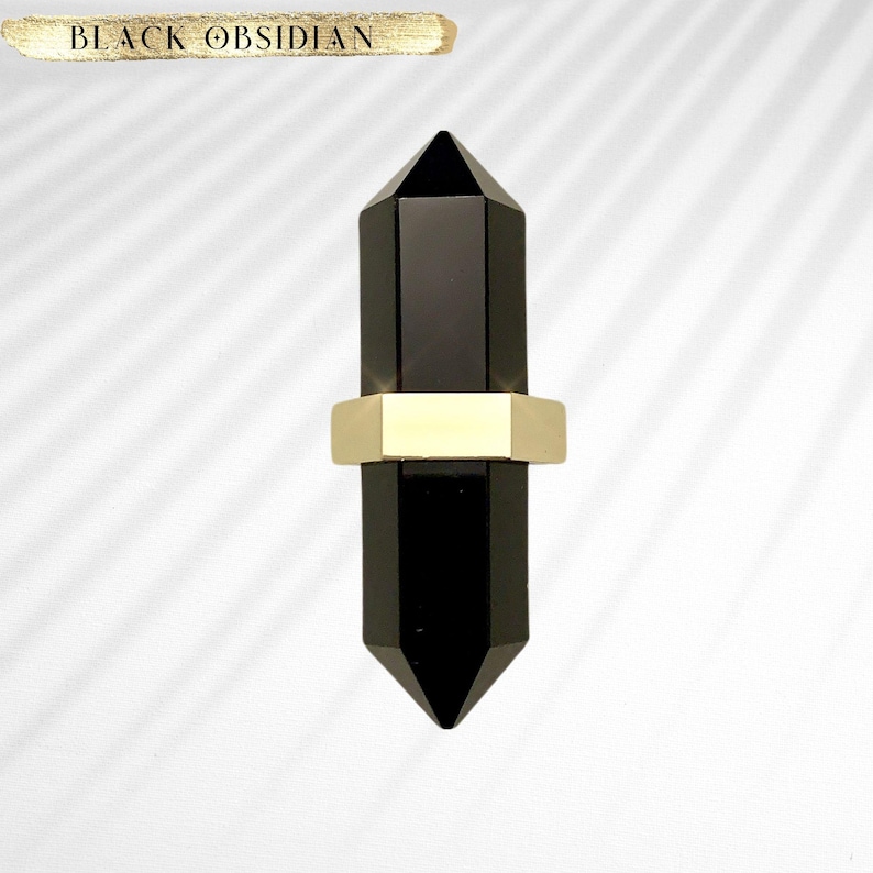 May include: Black obsidian crystal point with a gold hexagonal band. The crystal is a dark, opaque black and the band is a shiny, polished gold.