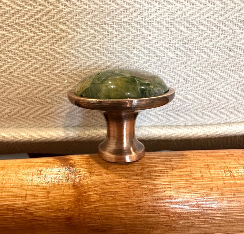 May include: A copper cabinet knob with a green marble top. The knob is round and has a mushroom-shaped base.