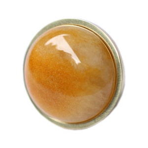 May include: A close-up of a round, golden-yellow gemstone ring. The gemstone has a polished, translucent appearance, set in a gold-colored metal band. The ring is set against a white background.