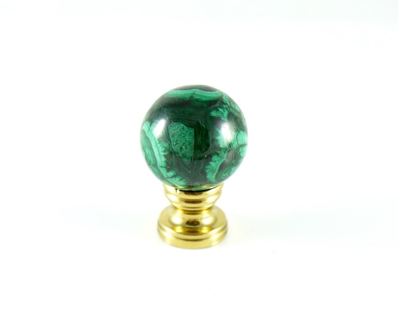 May include: A green malachite sphere knob with a gold metal base. The knob is a decorative element for furniture or cabinets.