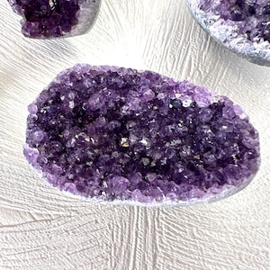 Pode incluir: Uma grande geoda de ametista com um aglomerado de cristais roxos. A geoda é lisa e tem uma forma natural irregular.