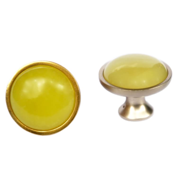 Puede incluir: Un par de pomos de armario de vidrio amarillo con un borde de metal dorado. El pomo de la derecha est&aacute; montado sobre una base de metal plateado.