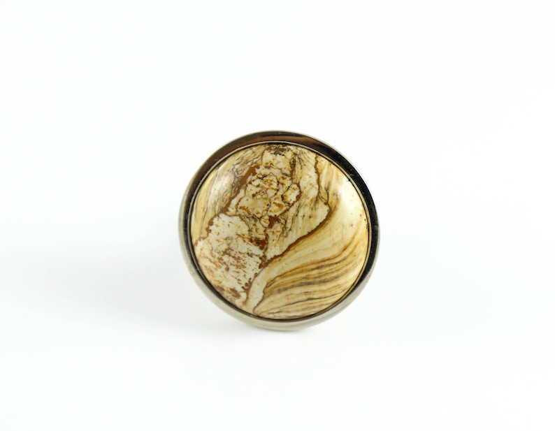 May include: A round, brown and white marbled knob with a silver metal rim.