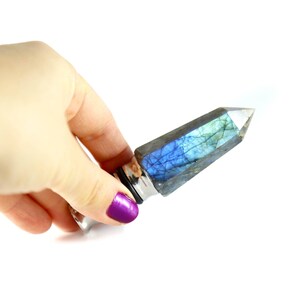 Puede incluir: Un tap&oacute;n de botella de cristal plateado y azul con una punta puntiaguda. El cristal es iridiscente y tiene un color azul y verde.