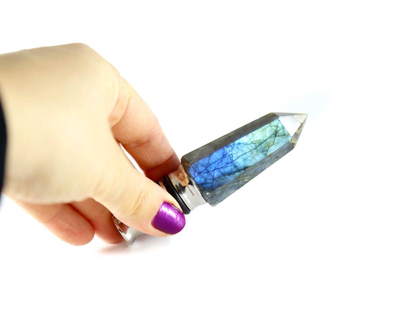Puede incluir: Un tap&oacute;n de botella de cristal plateado y azul con una punta puntiaguda. El cristal es iridiscente y tiene un color azul y verde.
