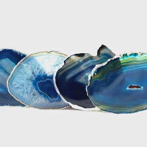 May include: Four blue agate coasters with unique patterns and colors. The coasters are round, with a polished surface and a natural, organic edge. The colors range from deep navy to light blue, with some areas of white and yellow.