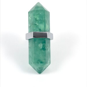 May include: A green crystal point with a silver metal band around the middle. The crystal is shaped like a long, thin pyramid.