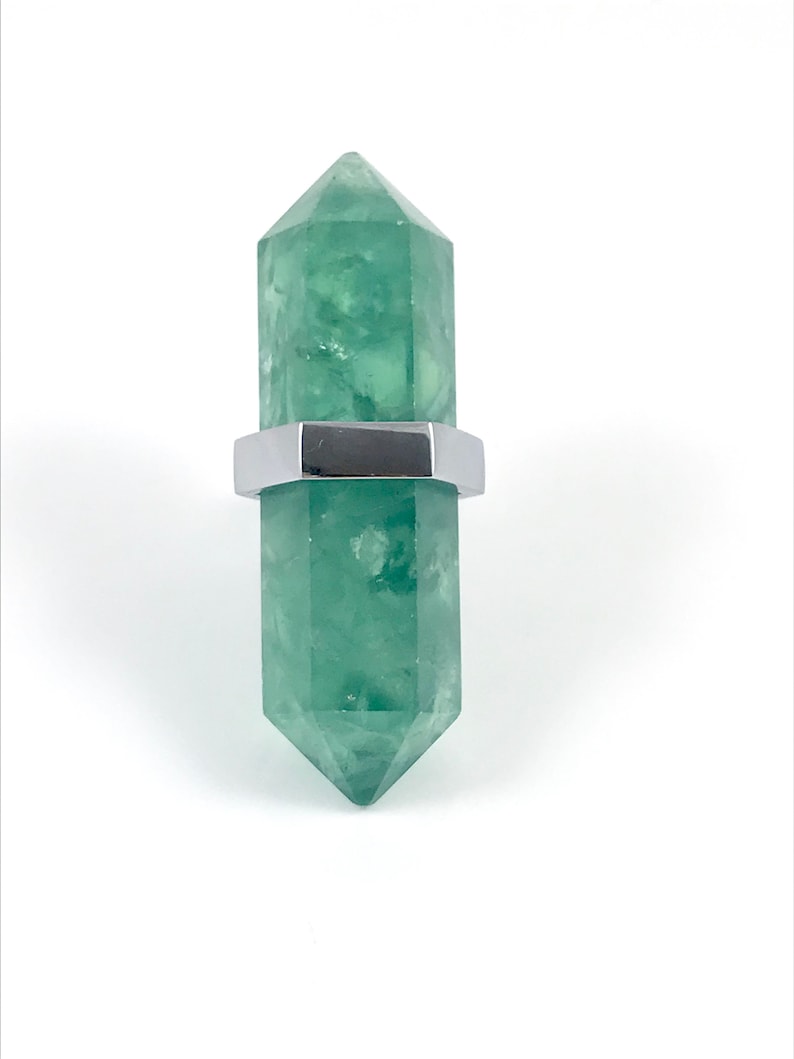 May include: A green crystal point with a silver metal band around the middle. The crystal is shaped like a long, thin pyramid.