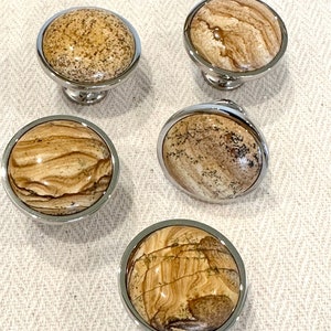 May include: Set of four round cabinet knobs with a polished chrome finish and a natural stone inlay. The stone has a brown and beige color with a swirling pattern.