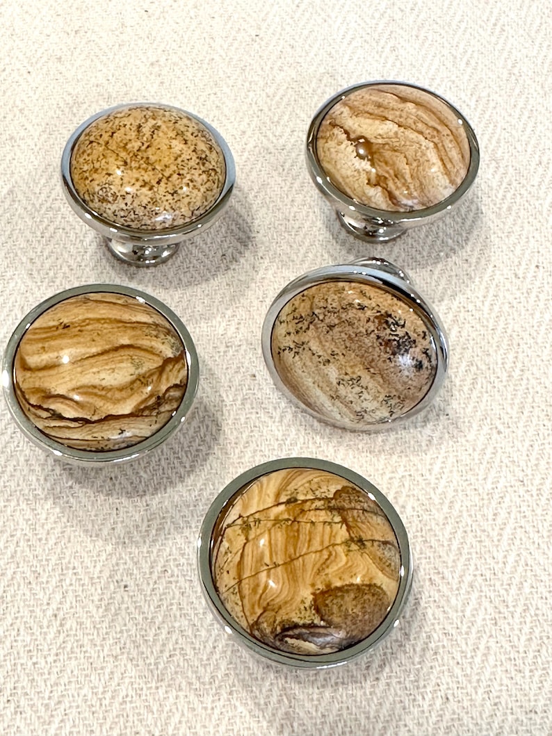 May include: Set of four round cabinet knobs with a polished chrome finish and a natural stone inlay. The stone has a brown and beige color with a swirling pattern.