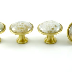 K&ouml;nnte beinhalten: Vier goldene Schrankkn&ouml;pfe mit wei&szlig;en Achat-Steinoberfl&auml;chen. Die Kn&ouml;pfe sind rund und haben eine glatte, polierte Oberfl&auml;che.