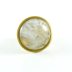 K&ouml;nnte beinhalten: Ein runder, wei&szlig;er und goldener Schrankknopf mit Marmormuster.