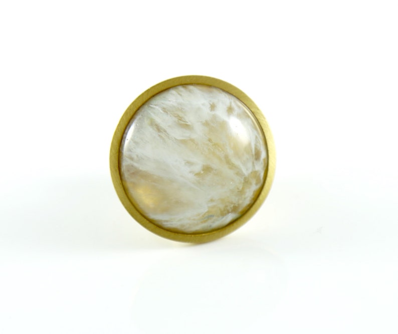 K&ouml;nnte beinhalten: Ein runder, wei&szlig;er und goldener Schrankknopf mit Marmormuster.