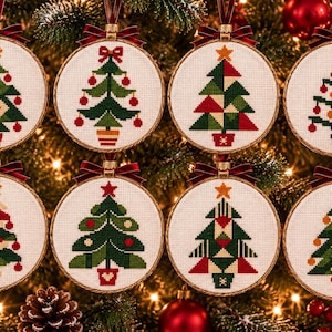 Op de afbeelding: Acht ronde borduurringen met kruissteekontwerpen van kerstbomen in diverse groene, rode en witte patronen. Elke ring is voorzien van een klein donkerrood fluwelen strikje om het ornament in de boom op te hangen.