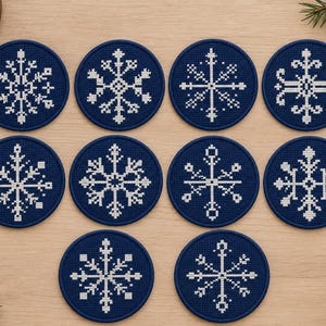 May include: A set of ten circular navy blue coasters featuring unique white cross-stitch snowflake patterns. Each coaster displays a distinct geometric winter design, showcasing intricate needlework details on a dark fabric background.