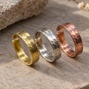 May include: Three open-ended rings featuring a hammered texture. The set includes one gold-toned ring, one silver-toned ring, and one copper-toned ring. Each band has a consistent width and a visible gap, allowing for slight adjustments in fit.