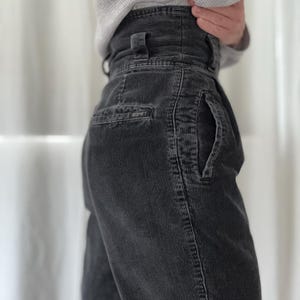 Può includere: Pantaloni a vita alta in velluto a coste grigio antracite con tessuto testurizzato, passanti per cintura e una tasca laterale. Una piccola etichetta rettangolare con la scritta ESPRIT è cucita sopra la tasca. Vestibilità strutturata.