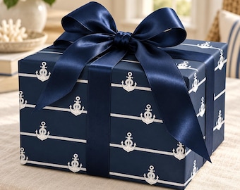 Könnte beinhalten: Eine rechteckige Geschenkbox, eingewickelt in dunkelblaues Papier mit einem sich wiederholenden weißen Muster aus Ankern und horizontalen Seillinien. Die Box ist mit einer großen, breiten, dunkelblauen Satin-Schleife auf der Oberseite verziert.