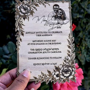 May include: A rectangular wooden wedding invitation featuring laser-engraved floral corners, a portrait of a couple, and text reading Mike & Dede, Joyfully invite you to celebrate their marriage, Saturday, 12 June 2027, The Grand Willow Estate, Charleston, South Carolina.