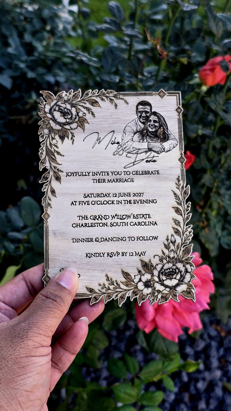 May include: A rectangular wooden wedding invitation featuring laser-engraved floral corners, a portrait of a couple, and text reading Mike & Dede, Joyfully invite you to celebrate their marriage, Saturday, 12 June 2027, The Grand Willow Estate, Charleston, South Carolina.