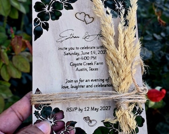 May include: A rectangular wooden wedding invitation card featuring black hibiscus flower illustrations, two heart outlines, and two ring icons. The text reads Ethan & A, Saturday, June 14, 2027, at 4:00 PM, Coyote Creek Farm, Austin, Texas, and RSVP by 12 May 2027.