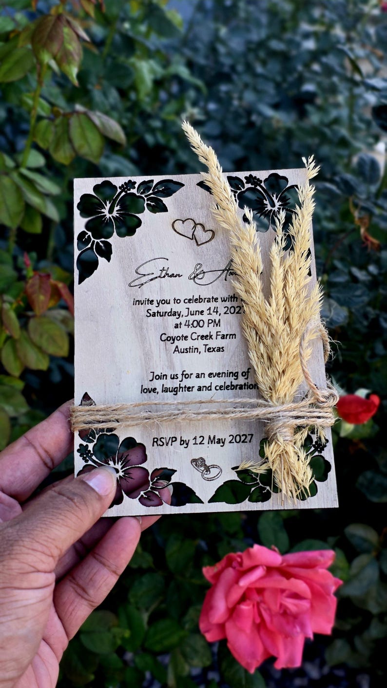 Peut inclure: Une carte d'invitation de mariage rectangulaire en bois avec des illustrations d'hibiscus noirs, deux c&oelig;urs et deux anneaux. Le texte indique Ethan & A, samedi 14 juin 2027, 16h00, Coyote Creek Farm, Austin, Texas, et RSVP avant le 12 mai 2027.