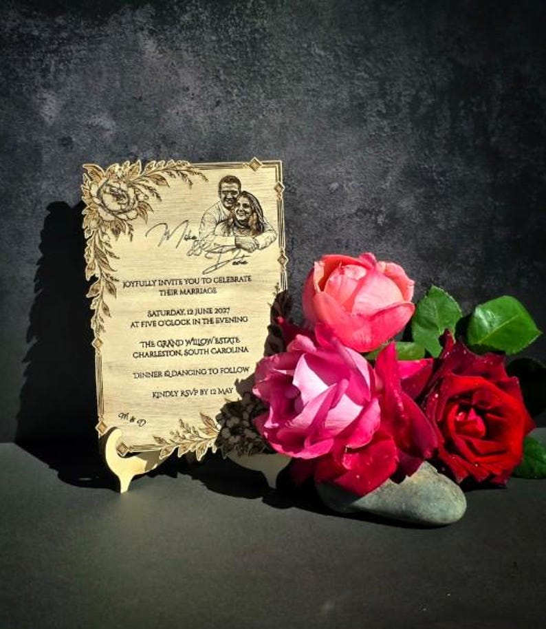 May include: A rectangular wooden wedding invitation plaque featuring a laser-engraved portrait of a couple, floral borders, and text detailing a marriage celebration on Saturday, 12 June 2027, at The Grand Willow Estate in Charleston, South Carolina.