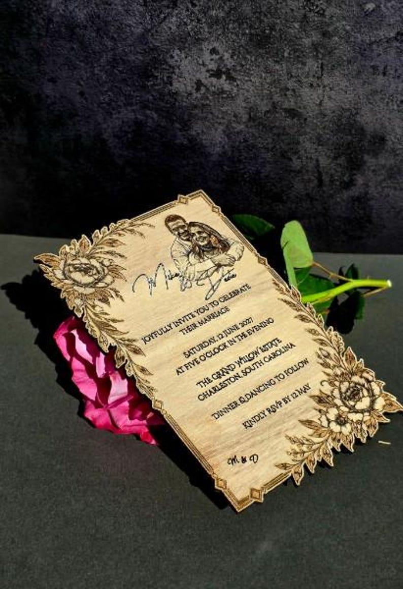 May include: A rectangular wooden wedding invitation with laser-engraved floral borders, a portrait of a couple, and text reading: Joyfully invite you to celebrate their marriage, Saturday, 12 June 2027, The Grand Willow Estate, Charleston, South Carolina.