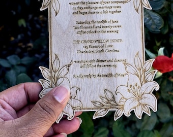 May include: A rectangular wooden wedding invitation with laser-engraved lily floral corners and text reading: Together with their families MARK & JACKIE request the pleasure of your company as they exchange marriage vows and begin their new life together.