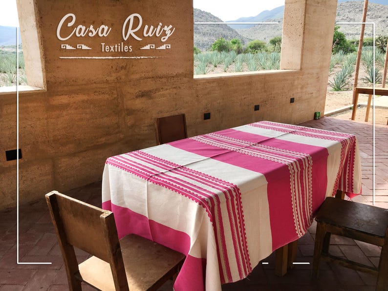 May include: A rectangular tablecloth featuring alternating wide stripes of vibrant hot pink and off-white fabric. The design includes intricate woven detailing with thin pink lines and decorative borders. The text Casa Ruiz Textiles is visible.