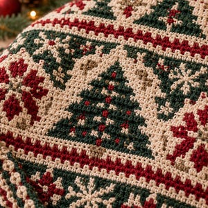 Op de afbeelding: Een gehaakt textiel met een herhalend patroon van donkergroene kerstbomen en rode sneeuwvlokken op een crèmekleurige achtergrond. Het ontwerp bestaat uit dichte, gestructureerde steken die in horizontale banen zijn gerangschikt.