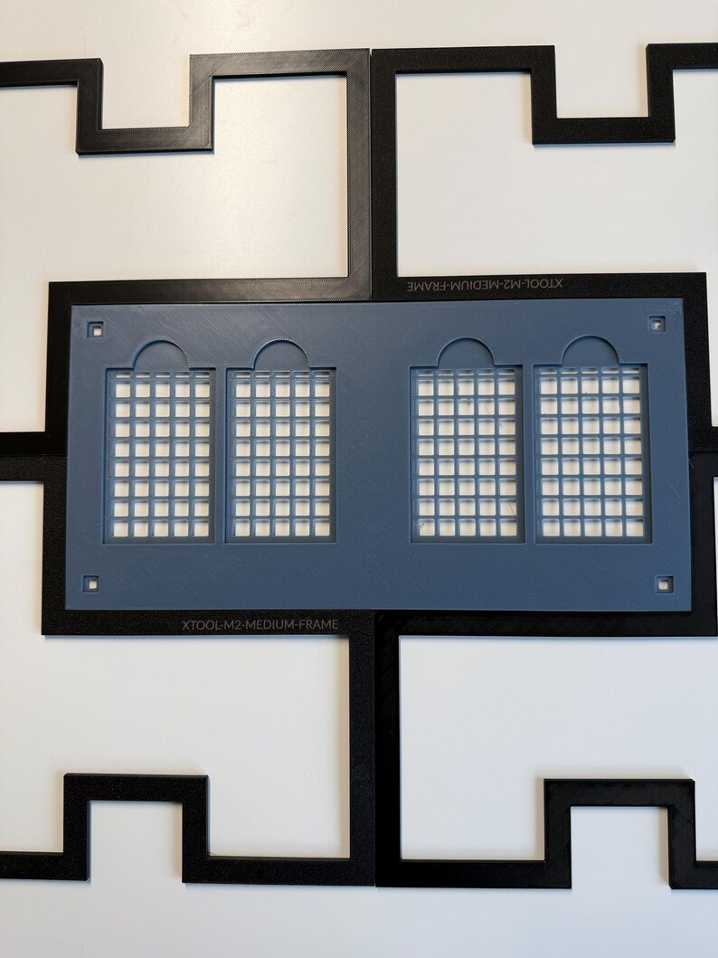 Może przedstawiać: Czarna ramka XTOOL-M2-MEDIUM-FRAME z geometrycznym, zazębiającym się wzorem obramowania otaczającym centralną niebieską prostokątną wkładkę. Niebieska wkładka posiada cztery łukowate wycięcia okienne z siatką i małe kwadratowe otwory.