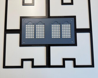 May include: A black xTool M2 medium frame consisting of four interlocking pieces arranged in a rectangular shape. Centered within the frame is a gray rectangular plate featuring four grid-patterned windows and small circular holes at the corners.