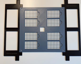 May include: A gray square grid plate with eight rectangular cutouts, flanked by two black rectangular frames labeled XTOOL M2 LARGE FRAME. The gray plate features a central square hole and a grid pattern, while the black frames have two rectangular openings each.