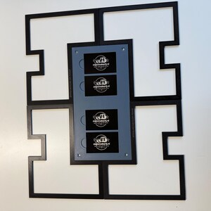 Może przedstawiać: Czarna ramka XTOOL M2 MEDIUM FRAME z centralną szarą prostokątną wkładką zawierającą cztery czarne prostokątne panele. Każdy panel zawiera białe logo i tekst 'mijnmakerij.nl'. Ramka ma geometryczny, zazębiający się wz&oacute;r.