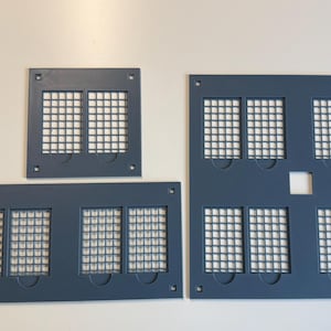 May include: Three dark gray rectangular panels featuring grid-patterned cutouts. The top left panel has two grid sections, the bottom left has four, and the large right panel contains eight grid sections with a small square hole in the center.
