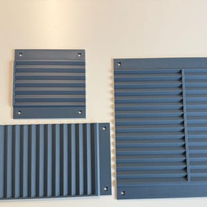 May include: Three dark gray rectangular ventilation grilles with horizontal slats and pre-drilled mounting holes in each corner. The set includes one large square grille, one smaller square grille, and one wide rectangular grille with vertical slats.