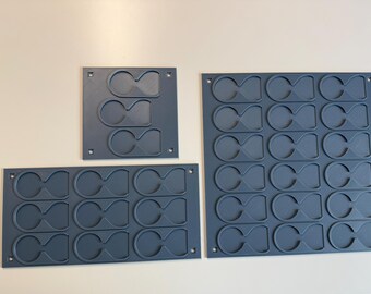May include: Three dark gray rectangular storage organizers with multiple recessed, figure-eight shaped slots. The organizers feature small square mounting holes in each corner, designed for holding small items in a grid-like arrangement.