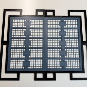 May include: A black rectangular frame with an intricate geometric border surrounds a gray grid insert. The gray insert features two vertical columns of five rectangular sections, each containing a small square grid pattern. The text XTOOL M2 FULL-RI FRAME is visible.