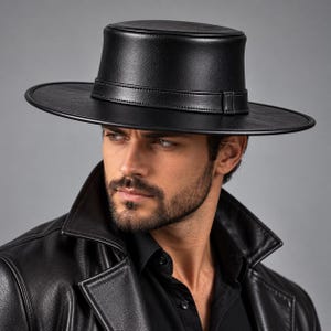 Puede incluir: Un sombrero negro de copa plana con ala ancha y una banda de aspecto de cuero a juego alrededor de la base. El sombrero presenta un acabado liso y estructurado con una silueta circular limpia, ofreciendo un aspecto audaz y clásico.