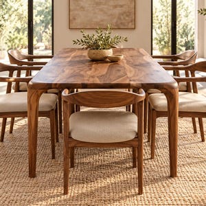 May include: A rectangular wooden dining table with rounded corners and six matching chairs. Each chair features a curved backrest and a light beige upholstered seat. The table and chairs are crafted from a medium-toned wood with visible grain.