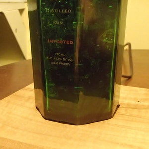 May include: A green glass bottle of gin with the word "IMPORTED" in red. The bottle is on a wooden cutting board. The bottle contains 750 mL of gin, 47.3% alcohol by volume (94.6 proof).