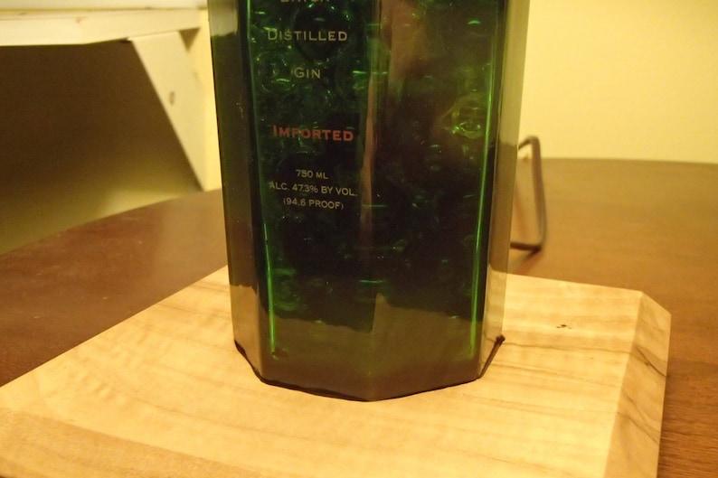 May include: A green glass bottle of gin with the word "IMPORTED" in red. The bottle is on a wooden cutting board. The bottle contains 750 mL of gin, 47.3% alcohol by volume (94.6 proof).