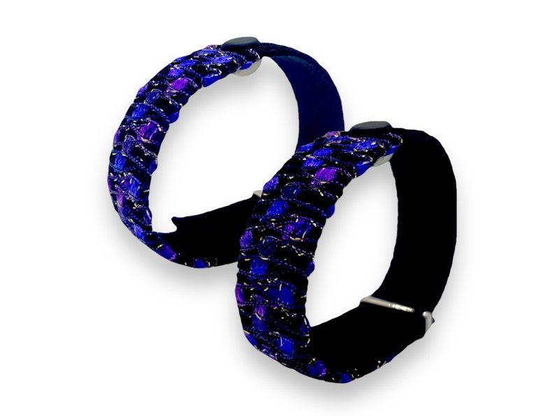 K&ouml;nnte beinhalten: Zwei Armb&auml;nder mit einem schwarzen Samtband und einem gewebten Design in Blau-, Lila- und Silbert&ouml;nen. Die Armb&auml;nder haben einen Verschluss und ein dekoratives Webmuster.