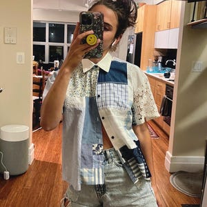 Könnte beinhalten: Ein blaues und weißes Patchwork-Shirt mit weißem Kragen und kurzen Ärmeln. Das Shirt ist offen und die Person, die es trägt, zeigt ihren Bauchnabel. Die Person trägt hellblaue Jeans-Shorts mit ausgefransten Kanten.