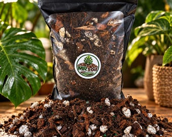 Pode incluir: Um saco plástico preto cheio de substrato tropical grosso, com uma etiqueta branca circular com o texto MR soil e um gráfico de folha verde. O saco está posicionado atrás de uma pilha da mesma terra castanha escura, lascas de madeira e perlite branca.