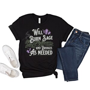May include: Black t-shirt with a white graphic that says "Will Burn Sage and Bridges As Needed". The graphic also includes a purple crystal and a bundle of sage.